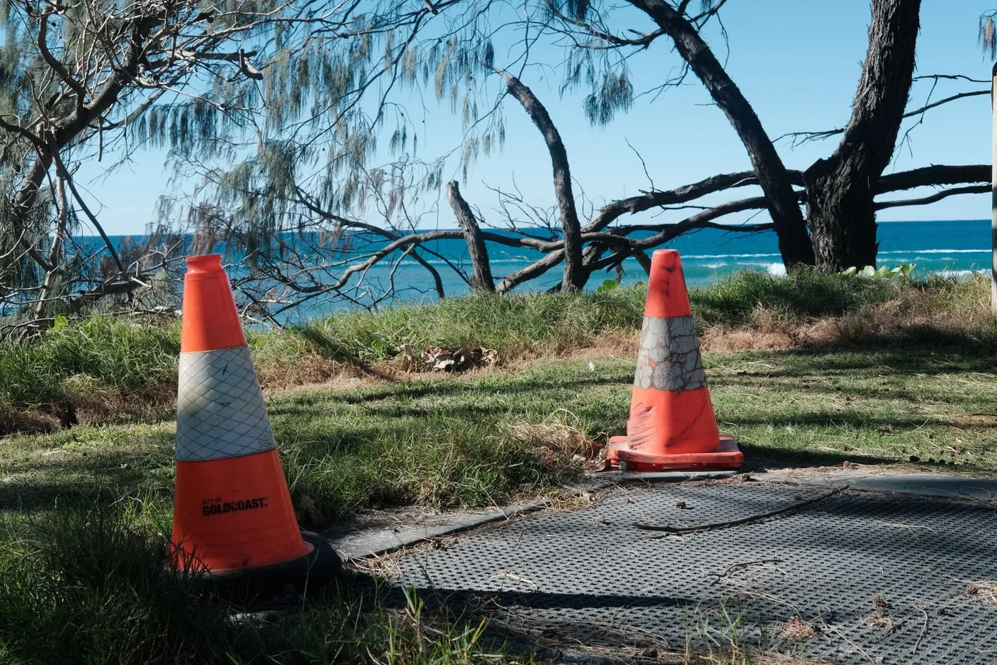 Two orange traffic cones on the grass by the sea